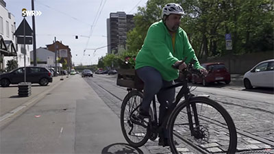 Fahrradfahrer in grüner Jacke mit Helm in einer Stadt mit Straßenbahnschienen