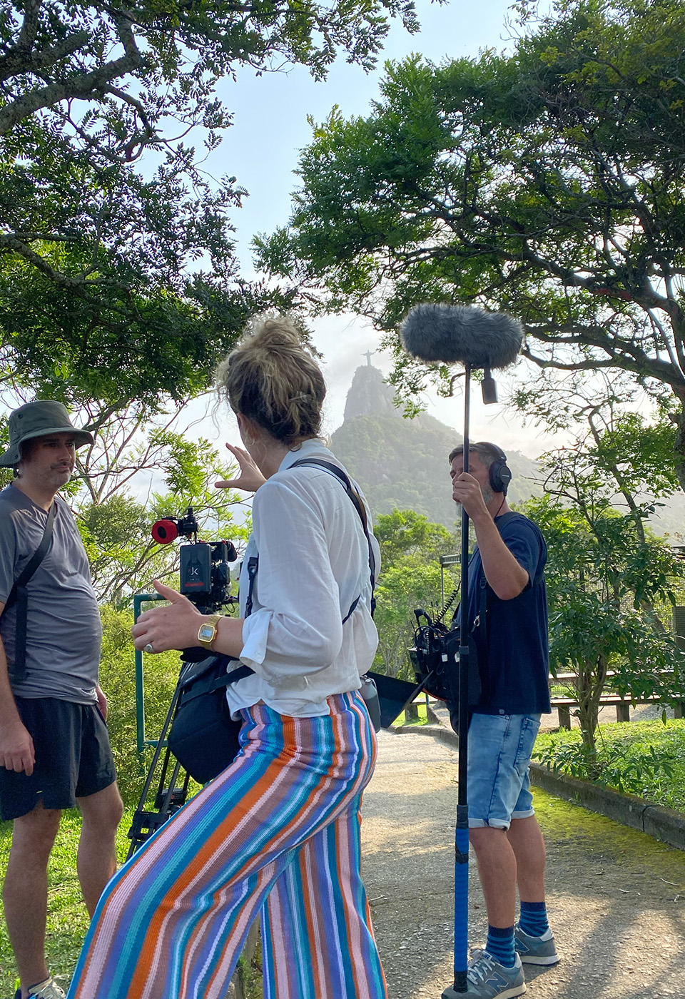 Ein Filmteam dreht draußen in einem grünen Park mit Blick auf eine bekannte Statue im Hintergrund.