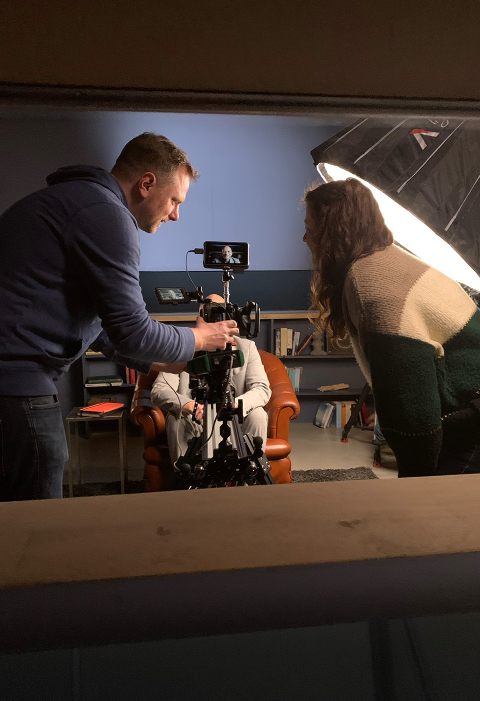 Zwei Crewmitglieder filmen ein Interview; ein Mann sitzt auf einem Ledersessel unter Studio-Beleuchtung.
